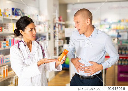 Man complains to a pharmacist about a sore belly. Help in choosing a medicine in pharmacy Man complains to a pharmacist about a sore belly. Help in choosing a medicine in pharmacy 91457936