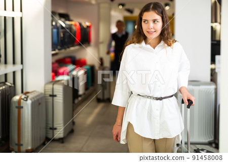 Portrait of woman with suitcase on wheels after shopping in haberdashery store 91458008