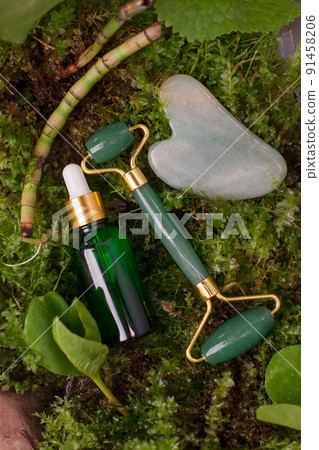 Green Jade roller, gua sha stone for face with serum, face oil on natural forest background. Facial massage set. The concept of Organic natural cosmetics, beauty, anti-age, banner for salon 91458206