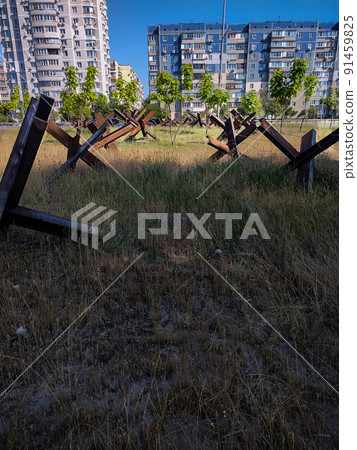 Iron anti-tank structures on the background of city buildings. 91459825