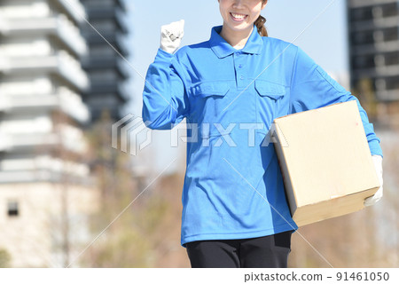 A woman in work clothes holding a cardboard box outdoors A woman in work clothes holding a cardboard box outdoors 91461050