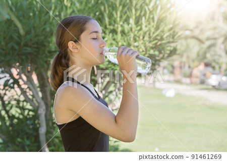 Sportswoman drinks water from a transparent plastic bottle. 91461269