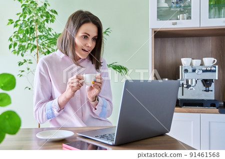 Joyful surprised woman looking at laptop screen, sitting at home in kitchen 91461568