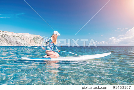 Healthy happy fit woman in bikini relaxing on a sup surfboard, floating on the clear turquoise sea water. Recreational Sports. Stand Up Paddle boarding. Summer fun, holidays travel. Active lifestyle 91463197