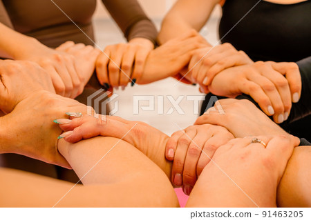 Partnership and unity concept: unrecognizable women in sportswear holding wrists of each other, forming circle. Group of happy young women holding hands. Side view on human hands. Partnership and unity concept: unrecognizable women in sportswear holding wrists of each other, forming circle. Group of happy young women holding hands. Side view on human hands. 91463205