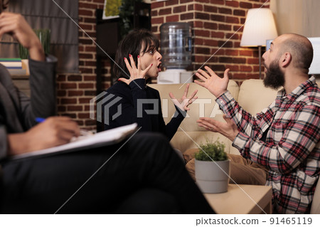 Angry partners fighting at couple therapy session with specialist, having argument about marriage difficulties. Trying to solve relationship issues with professional help and advice from therapist. Angry partners fighting at couple therapy session with specialist, having argument about marriage difficulties. Trying to solve relationship issues with professional help and advice from therapist. 91465119