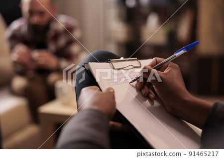 Male psychologist taking notes at couple therapy session to help with relationship issues, counselor giving advice. Explaining marriage problems, using paper to do psychoanalysis. Close up, 91465217