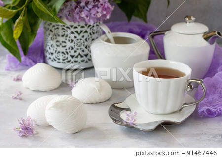 Delicate vanilla marshmallow on a white delicate plate. Still life with marshmallows, a cup of tea and lilac lilac on a background of ancient stone. Delicate vanilla marshmallow on a white delicate plate. Still life with marshmallows, a cup of tea and lilac lilac on a background of ancient stone. 91467446