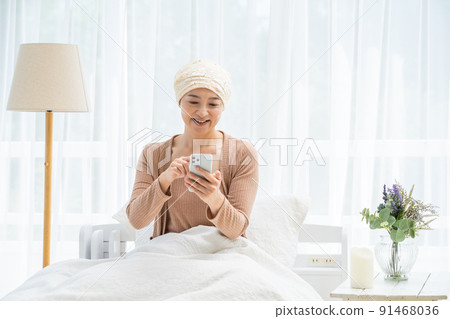 一位戴著醫用帽子的中年婦女在床上看著她的智能手機 一位戴著醫用帽子的中年婦女在床上看著她的智能手機 91468036