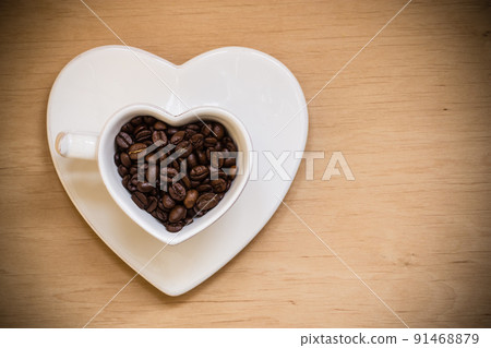 Heart shaped cup with coffee beans on wooden table Heart shaped cup with coffee beans on wooden table 91468879