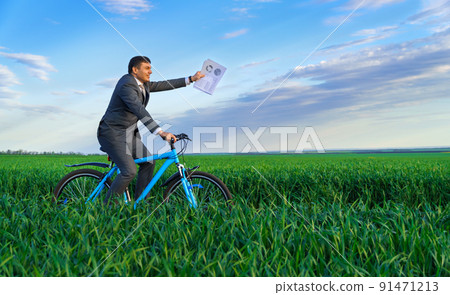 businessman dressed in a business suit, rides with reports or documents a bicycle through a green grass field, beautiful nature in spring, business concept 91471213