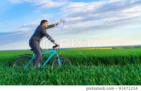businessman dressed in a business suit, rides with reports or documents a bicycle through a green grass field, beautiful nature in spring, business concept 91471214