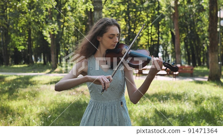 A young girl plays the violin in the city park. 91471364