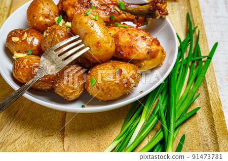 tasty lunch in rural style, healthy food - fried chicken meat and unpeeled roasted potatoes on a dish, green leek, salt and garlic, cooked food on a white wooden boards tasty lunch in rural style, healthy food - fried chicken meat and unpeeled roasted potatoes on a dish, green leek, salt and garlic, cooked food on a white wooden boards 91473781