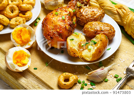tasty and healthy food, lunch in rural style - fried chicken meat and unpeeled potatoes, eggs, green leek, salt and garlic, cooked food on a wooden kitchen board 91473803