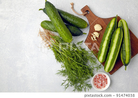 Fresh cucumbers peeled and sliced on a brown wooden cutting board with a bunch of dill, garlic and pink salt Fresh cucumbers peeled and sliced on a brown wooden cutting board with a bunch of dill, garlic and pink salt 91474038