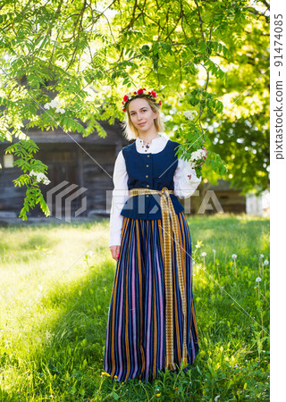 Latvian woman in traditional clothing posing on nature in village. 91474085