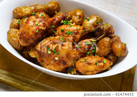 tasty lunch in rural style, healthy food - fried chicken meat and unpeeled roasted potatoes with chopped leeks in a big white dish, cooked food on a wooden background tasty lunch in rural style, healthy food - fried chicken meat and unpeeled roasted potatoes with chopped leeks in a big white dish, cooked food on a wooden background 91474435
