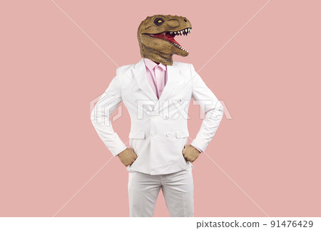 Portrait of a man in a funny dinosaur mask and a white suit standing on a pink background 91476429