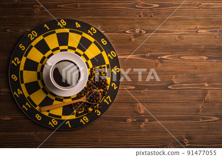 Cup of coffee on dart board on brown wooden table background. Composition with free space for text or design Cup of coffee on dart board on brown wooden table background. Composition with free space for text or design 91477055