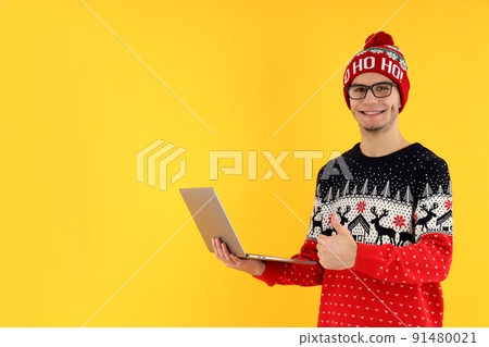 Guy in Christmas sweater with laptop on yellow background Guy in Christmas sweater with laptop on yellow background 91480021