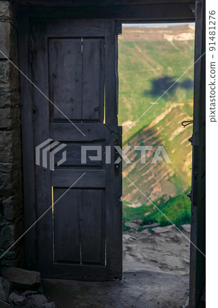 wooden door in the ruins of an abandoned house through which mountains are visible, in the ruins of the ghost village of Gamsutl in Dagestan 91481276