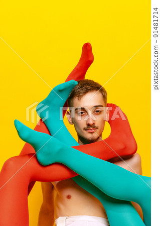 Creative colorful portrait of man with female legs in bright tights twining him isolated over yellow background. Extravagant. Creative colorful portrait of man with female legs in bright tights twining him isolated over yellow background. Extravagant. 91481714