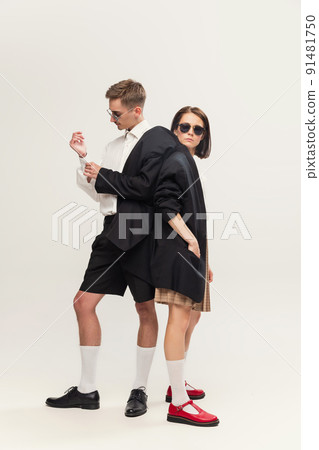 Full-length portrait of stylish young couple, man and woman standing in one jacket, posing isolated over grey studio background 91481750