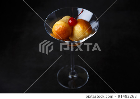 Neapolitan Rum baba (or baba au rum) in a martini glass with a cocktail cherry on a black background. Small yeast cakes soaked in rum syrup. Traditional Italian pastry. Close-up, selective focus. Neapolitan Rum baba (or baba au rum) in a martini glass with a cocktail cherry on a black background. Small yeast cakes soaked in rum syrup. Traditional Italian pastry. Close-up, selective focus. 91482268