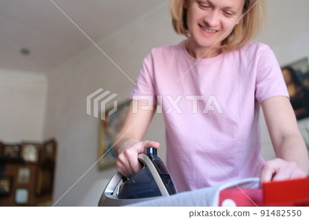 Happy woman ironing clothes with electric iron at home 91482550