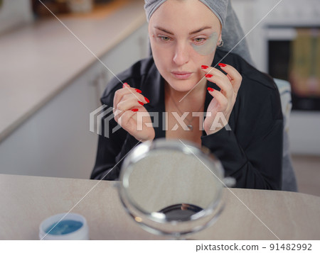 Young woman applies patches under eyes. Beauty and technology concept. 91482992