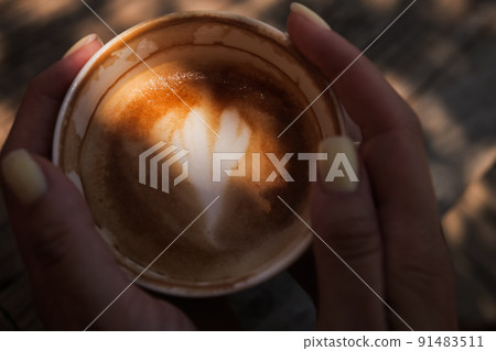 Woman hands holding cup of cappuccino coffee with heart shape. Woman hands holding cup of cappuccino coffee with heart shape. 91483511