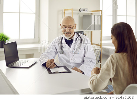 Senior male doctor at a clinic or hospital giving a consultation to a young woman Senior male doctor at a clinic or hospital giving a consultation to a young woman 91485108