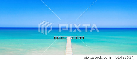 White wooden pier over bright turquoise sea water, panorama of tropical island coast White wooden pier over bright turquoise sea water, panorama of tropical island coast 91485534