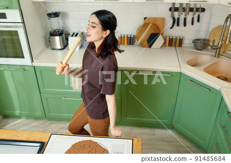 Young happy joyful brunette cooking homemade cookies while dancing 91485684