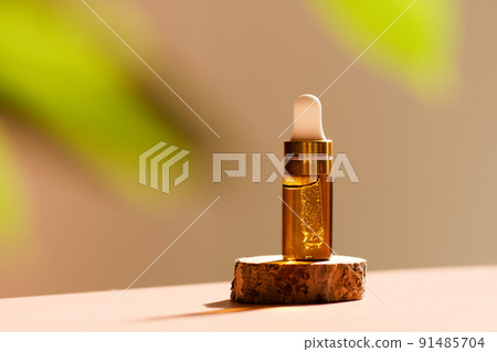 Cosmetic amber glass dropper bottle on wooden podium with oil, serum or fruit peeling in the sunlight. Green ruscus, soft focus. Beauty product presentation, natural background. Front. Mockup concept  91485704