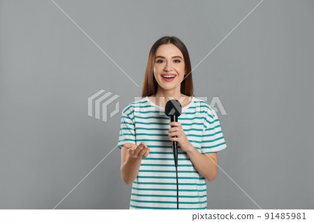 Young female journalist with microphone on grey background Young female journalist with microphone on grey background 91485981