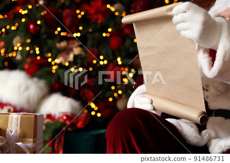 Santa Claus reading wish list against blurred festive lights, closeup Santa Claus reading wish list against blurred festive lights, closeup 91486731