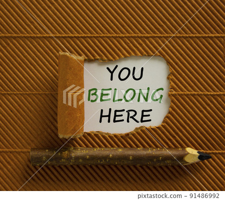Inclusion and belonging symbol. Words 'You belong here' appearing behind torn brown paper. Beautiful brown background. Business, better inclusion and belonging concept. Copy space. Inclusion and belonging symbol. Words 'You belong here' appearing behind torn brown paper. Beautiful brown background. Business, better inclusion and belonging concept. Copy space. 91486992