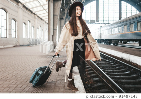 Cheerful young lady traveler is waiting for her train at the train station. Cheerful young lady traveler is waiting for her train at the train station. 91487145