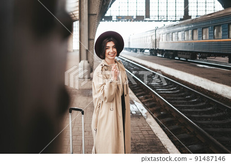 Beautiful stylish woman traveler stands on the peron of the station waiting for the train. Beautiful stylish woman traveler stands on the peron of the station waiting for the train. 91487146