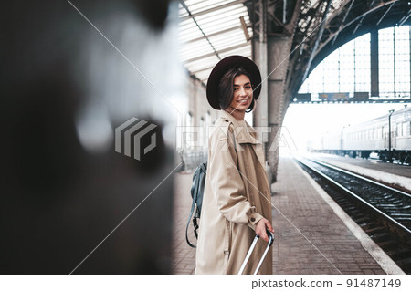 Beautiful stylish woman traveler stands on the peron of the station waiting for the train. Beautiful stylish woman traveler stands on the peron of the station waiting for the train. 91487149