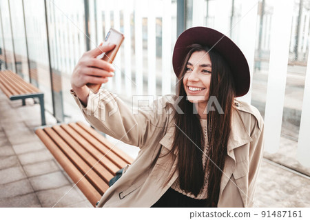 Stylish girl in hat makes selfie while sitting at a public bus stop. Stylish girl in hat makes selfie while sitting at a public bus stop. 91487161
