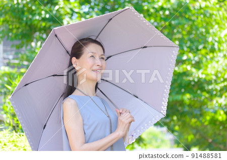 A smiling senior woman holding a parasol and taking measures against UV rays in a park with strong sunlight 91488581