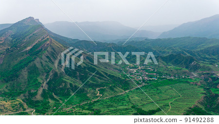 foggy highland valley with vliiage and fields between mountain peaks 91492288