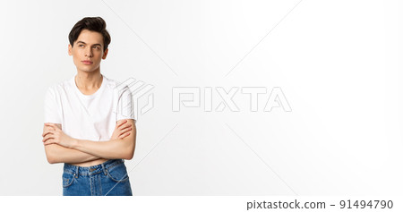 Thoughtful gay man in crop top looking at upper left corner, thinking with arms crossed on chest, standing against white background Thoughtful gay man in crop top looking at upper left corner, thinking with arms crossed on chest, standing against white background 91494790