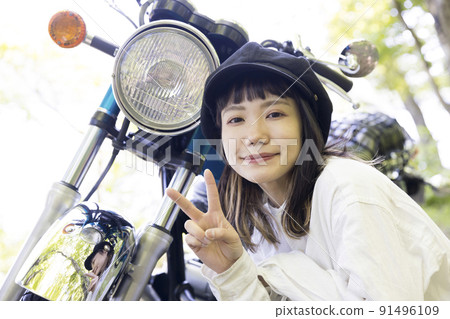 Bike girl image: A young woman sitting next to a motorcycle 91496109