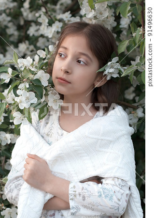 Portrait of a beautiful little girl in a light dress near a blooming apple tree. petals of a white apple tree. spring day 91496630