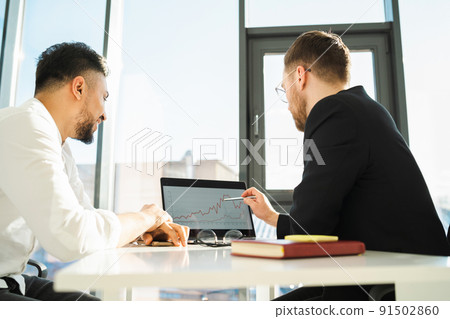 Two businessmen in the office analyze the profit of the company from the graph on the laptop Two businessmen in the office analyze the profit of the company from the graph on the laptop 91502860