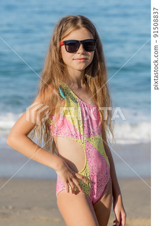 Girl posing on the beach in a pink swimsuit and glasses. 91508837